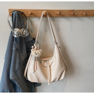 Detail of hobo shoulder bag in cream leather with plush bear charm on wooden hanger
