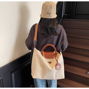 Detail of canvas tote bag showing leather handles, metal logo, and adjustable wide strap