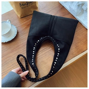 Détail du sac hobo en daim noir avec des clous en métal argenté poli sur un bureau en bois