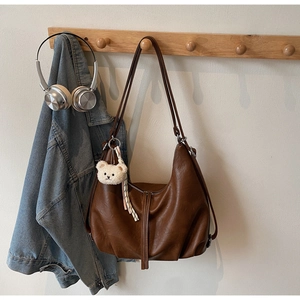 Brown faux leather crescent hobo bag hanging on hook with cute bear plush charm detail
