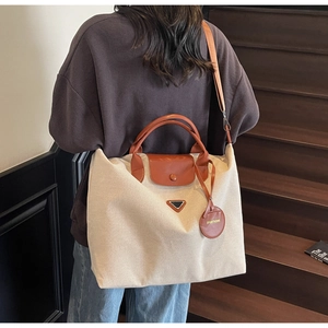 Detail of cream canvas tote bag with brown leather handles and adjustable crossbody strap