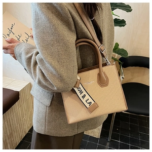 Détail du sac cabas en tissu beige avec bordure en cuir marron sur un blazer gris