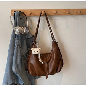 Close-up of brown faux leather hobo bag with fringe zippers and a cute plush bear charm