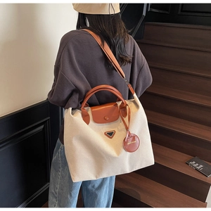 Detail of beige canvas tote with brown leather handles and triangle metal logo plaque