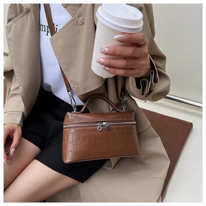 Detail of dark brown crocodile pattern leather handbag with crossbody strap and gold zippers