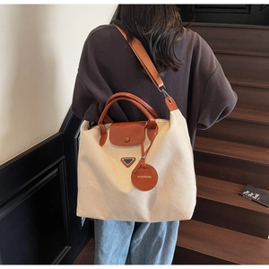 Detail of canvas tote bag with brown leather trim and metallic triangle plaque
