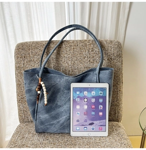 Close-up of a blue-grey tote bag with matte texture and boho beaded charm detail