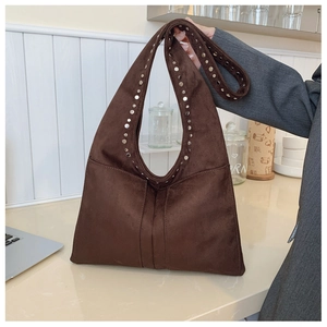 Détails des clous argentés sur un grand sac à bandoulière en daim marron porté à la main