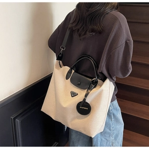 Detail shot of a large canvas tote bag with black leather straps worn by a model