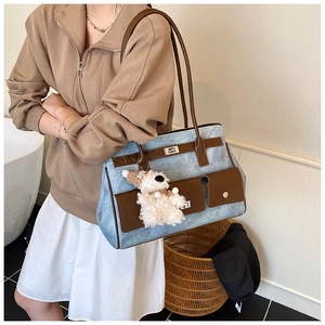 Detail of blue denim tote bag with brown faux leather trim and plush puppy pendant