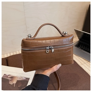 Detail of brown crocodile pattern handbag featuring silver dual zippers and top handle
