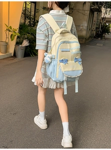 Lifestyle view of student backpack with blue bow and plush bear charm in street scene
