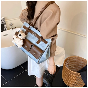 Detail of blue denim and brown leather tote bag with a plush bear charm on a model
