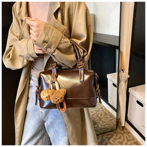 Detailed view of deep brown faux leather Boston bag with plush bear charm and metallic rings