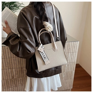 Gros plan du sac bandoulière beige en similicuir avec ruban décoratif sur modèle