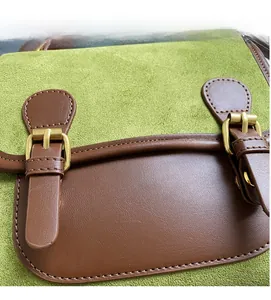 Close-up of matte green fabric texture and brown leather trim with golden metal buckles