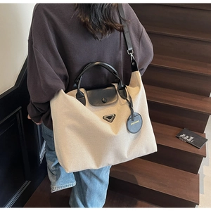 Close-up of canvas tote bag with black leather straps and metal triangle detail on a staircase