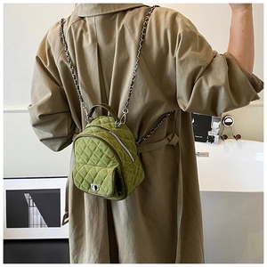 Olive green quilted mini backpack on model wearing khaki trench coat in modern setting
