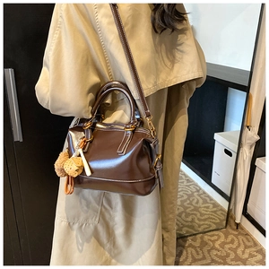 Detail of dark brown glossy Boston bag with gold hardware and plush charm on model