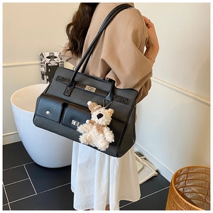 Detail view of large matte black tote bag with flap lock and white plush bear charm