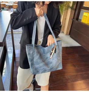 Detailed view of grey-blue leather tote bag with multi-color beaded tassel charm