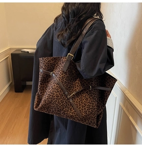 Detail of classic leopard print tote bag styled with a long black coat in indoor setting
