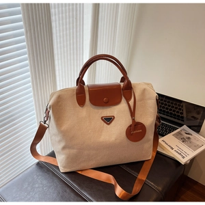 Detail of canvas travel tote featuring brown leather trim and triangle logo patch