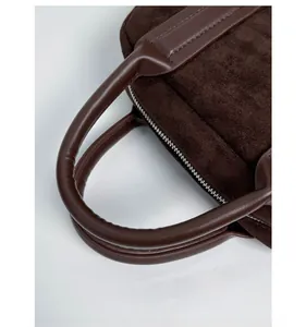 Detail of dark brown suede handbag with reinforced leather handles and silver zipper closure