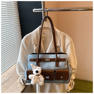 Detail of blue denim tote bag with brown leather trim and cute plush bear keychain
