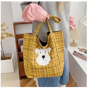 Detailed view of yellow plaid tote bag with white puppy patch carried by model