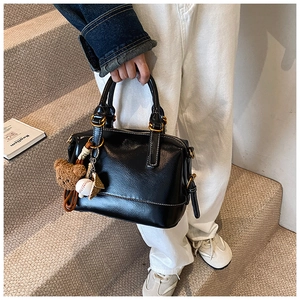 Detail of black glossy Boston bag with plush bear and baseball charms on top handle