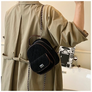 Close-up of quilted velvet mini backpack with chain strap on a model wearing a beige coat