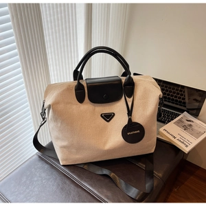 Detail of canvas tote bag showing black leather handles and metal triangle emblem