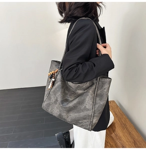 Detail of vintage gray tote bag with wrinkled texture and wooden bead charm on shoulder