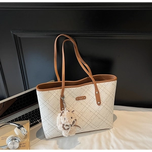 Dettaglio di una borsa tote beige con finiture in pelle marrone e ciondolo a coniglietto