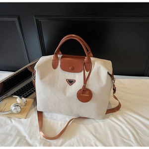 Close-up of cream canvas travel tote featuring brown leather trim and metal triangle logo