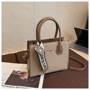 Détail du sac bandoulière en toile beige et cuir marron avec foulard en soie sur la poignée