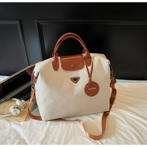 Close-up of beige canvas travel tote bag with brown leather handles and brand hardware