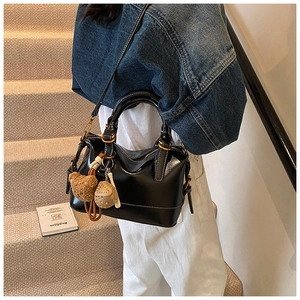 Detail of black glossy leather Boston bag featuring white stitching and bear charm