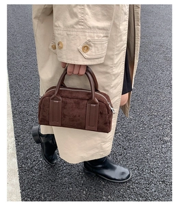 Detail of a brown suede bowling bag featuring dark leather handles and a sleek metal zipper