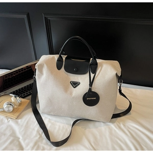Detailed close-up of a cream canvas tote bag with black leather accents and logo plate