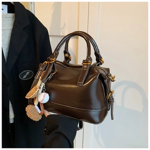 Detailed view of dark brown glossy boston bag with baseball charms and contrast stitching