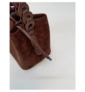 Detailed close-up of dark brown suede bucket bag with drawstring and chain handle