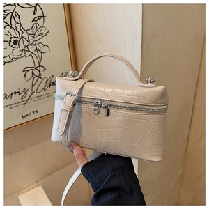 Detail of beige crocodile pattern box bag with dual silver zippers and top handle