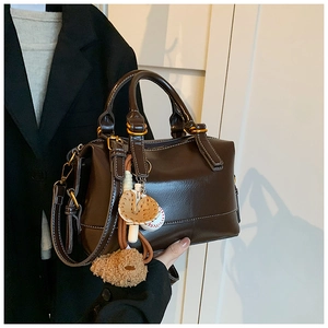 Detail of dark brown leather Boston bag with gold hardware and plush bear charm decoration