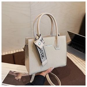 Détail d'un sac carré beige avec panneau en tissu texturé et foulard en soie décoratif