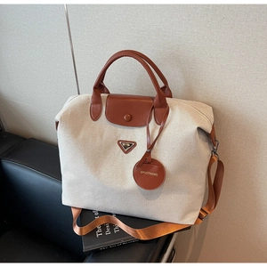 Close-up of a large beige canvas travel tote bag with brown leather handles and strap