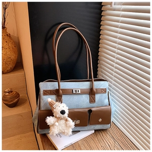 Detail of blue denim tote bag with brown leather trim and cute bear charm on a table