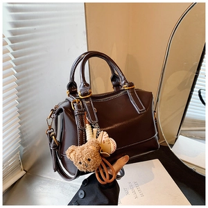 Detail of dark brown wax leather pillow bag with plush bear charm and golden hardware