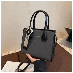 Détail d'un sac cabas tissé gris avec anses noires et bandoulière en cuir au bureau